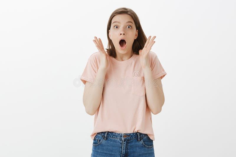 It is miracle, I am amazed. Portrait of surprised and pleased good-looking girl, dropping jaw, holding palms near face