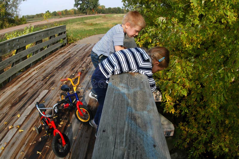 After parking their bikes, a young girl and boy take a look at what lays under a bridge. After parking their bikes, a young girl and boy take a look at what lays under a bridge.