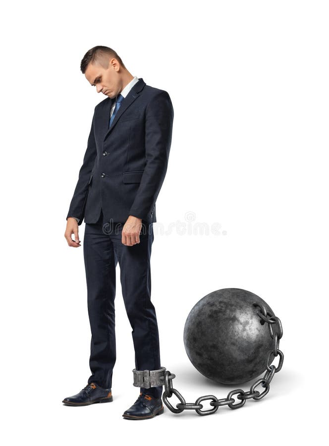 Miradas tristes de un hombre de negocios abajo mientras que está shackled a una bola grande del hierro con una cadena a su tobill fotografía de archivo Miradas tristes de un hombre de negocios abajo mientras que está shackled a una bola grande del hierro con una cadena a su tobill fotografía de archivo