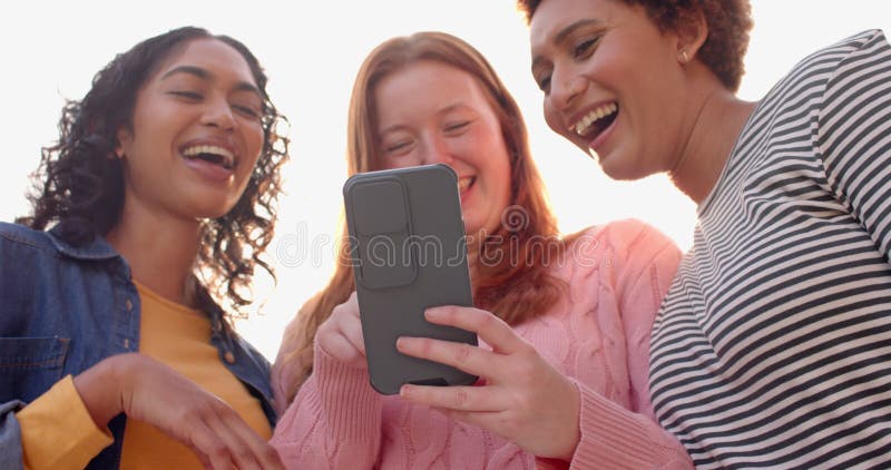 Mirando el smartphone, varias amigas se ríen juntas durante el hangout almacen de metraje de vídeo