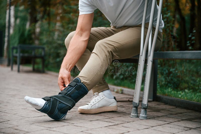 Mirando la pierna rota. hombre con muletas está en el parque al aire libre. lesión en la pierna.