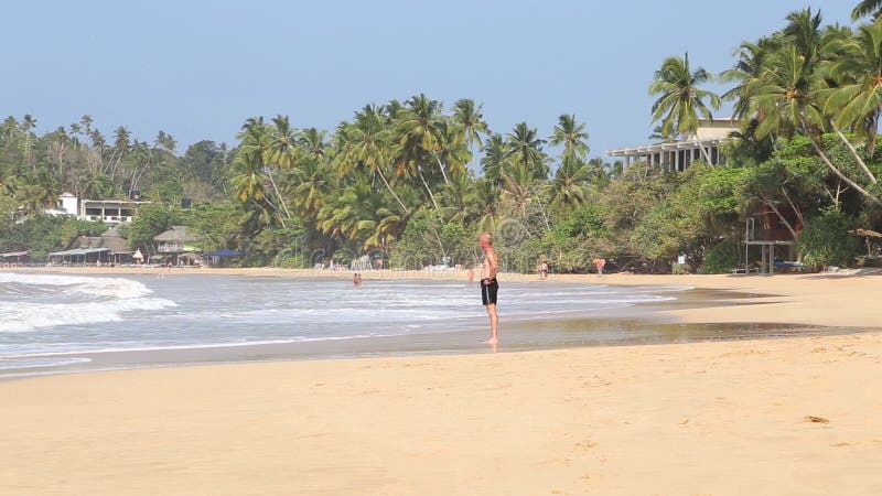 MIRISSA SRI LANKA - MARS 2014: Man anseendet i vågorna som tvättar sig upp på kust i Mirissa Skryt för denna små sandiga tropiska
