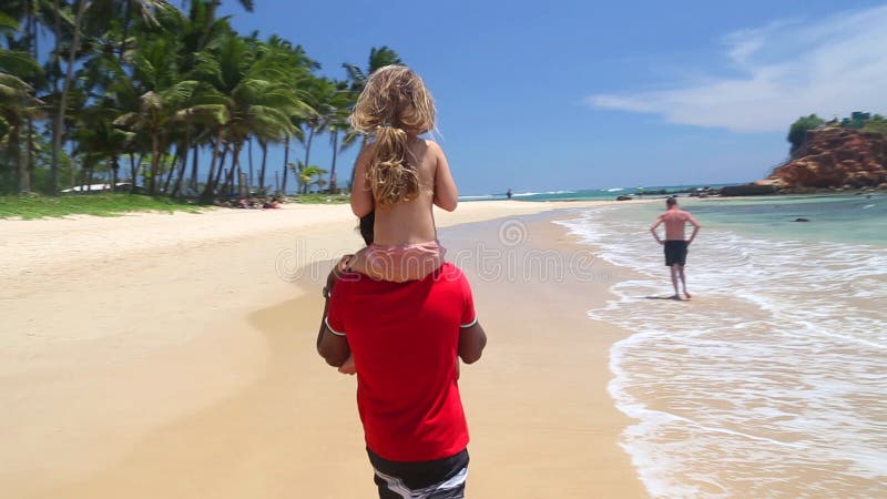 MIRISSA SRI LANKA - MARS 2014: Man den bärande lilla flickan på hans skuldror på stranden Denna lilla tropiska strand skryter någ