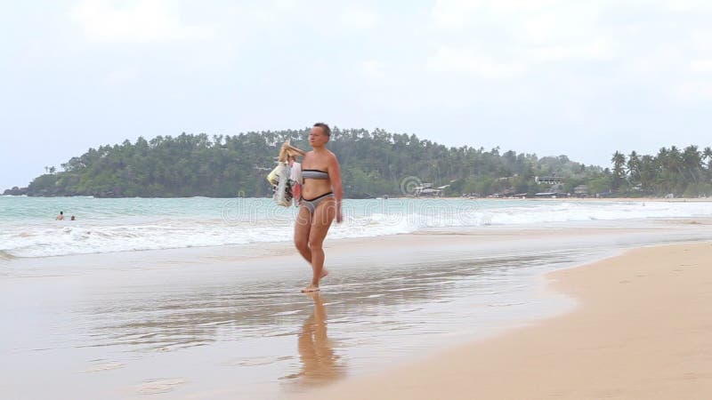 MIRISSA SRI LANKA - MARS 2014: Turister som går förbi på den sandiga stranden barfota med skor i deras händer Detta lilla sandiga