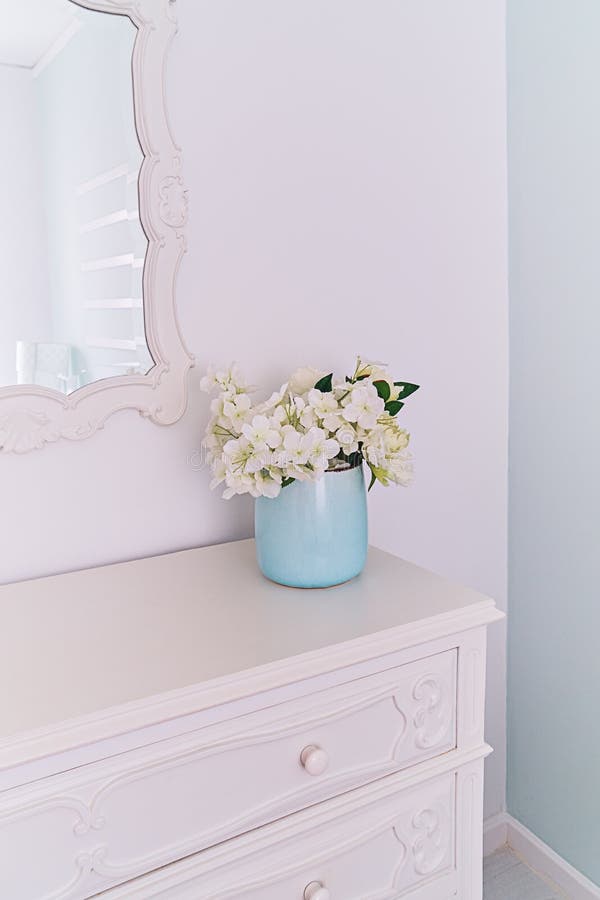 Mirror in carved wooden frame and vase with flowers in light room, vintage interior.