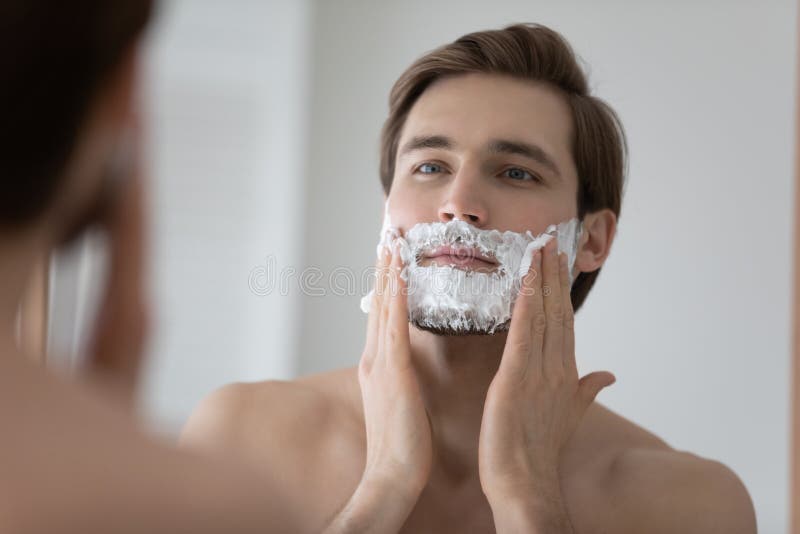 Mirror reflection close up young man applying shaving foam