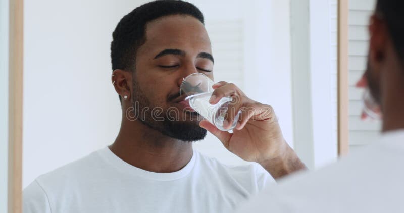 Young sleepy african american man drinking pure fresh mineral water.