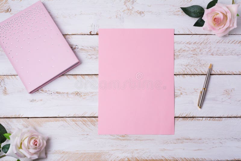 Miscela di carta bianca con rose. Foglio di carta di colore rosa in bianco, imbottito di taccuino, penna e rose sulla tavola di legno bianco