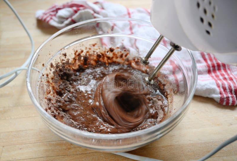 Miscelatore elettrico nell'azione che mescola pasta per il dolce di cioccolato in una ciotola di vetro, mosso, concetto di cottur fotografia stock libera da diritti Miscelatore elettrico nell'azione che mescola pasta per il dolce di cioccolato in una ciotola di vetro, mosso, concetto di cottur fotografia stock libera da diritti