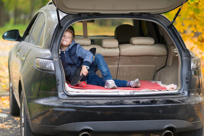 Mischievous little boy with a skateboard sitting in the trunk of a car grinning happily at the camera outdoors in a street in stock image Mischievous little boy with a skateboard sitting in the trunk of a car grinning happily at the camera outdoors in a street in stock image