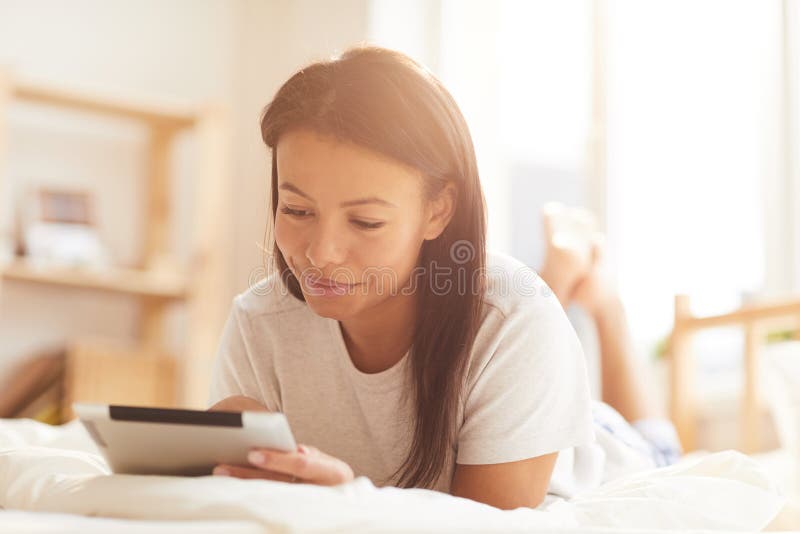 Mischrassefrau, die Tablette auf Bett verwendet lizenzfreies stockbild Mischrassefrau, die Tablette auf Bett verwendet lizenzfreies stockbild