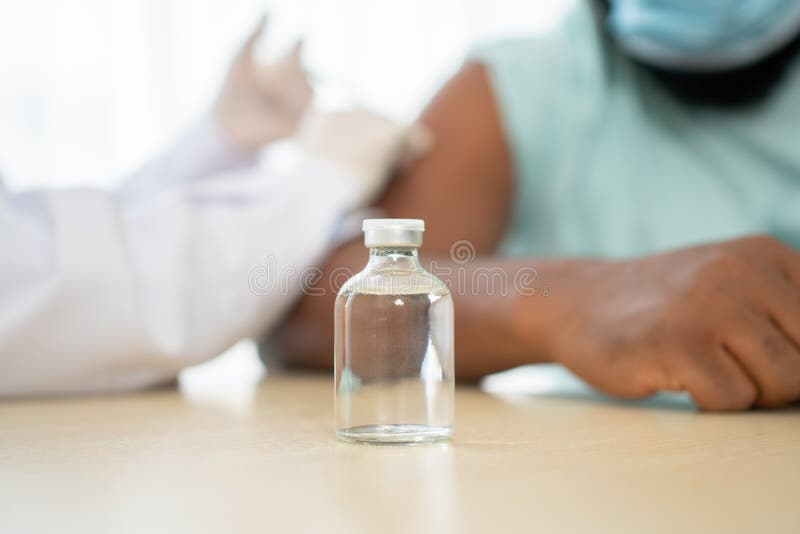 Selective focus of Vaccine bottle, African American Wear a medical mask and being covid vaccinated for the prevention of coronavirus and flu. Concept of immunization from inoculation. Selective focus of Vaccine bottle, African American Wear a medical mask and being covid vaccinated for the prevention of coronavirus and flu. Concept of immunization from inoculation