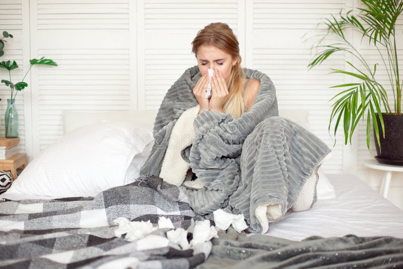 Miserable young woman sitting on the bed wrapped in warm blanket feeling sick with flu. stock photography Miserable young woman sitting on the bed wrapped in warm blanket feeling sick with flu. stock photography