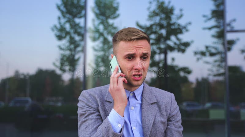 Missnöjd man som pratar på mobiltelefonen i staden. långsam rörelse royaltyfri bild