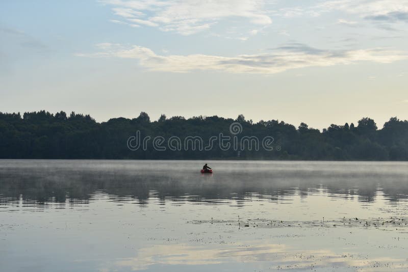 Mistige dageraad op de rivier, een eenzame visser van een boot die, weerspiegeld bos en wolken vissen stock foto's Mistige dageraad op de rivier, een eenzame visser van een boot die, weerspiegeld bos en wolken vissen stock foto's