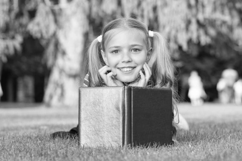 Mistura de fantasia e realidade Garota feliz lê livro de fantasia sobre grama verde Pequena criança desfruta da história da fanta fotografia de stock royalty free Mistura de fantasia e realidade Garota feliz lê livro de fantasia sobre grama verde Pequena criança desfruta da história da fanta fotografia de stock royalty free