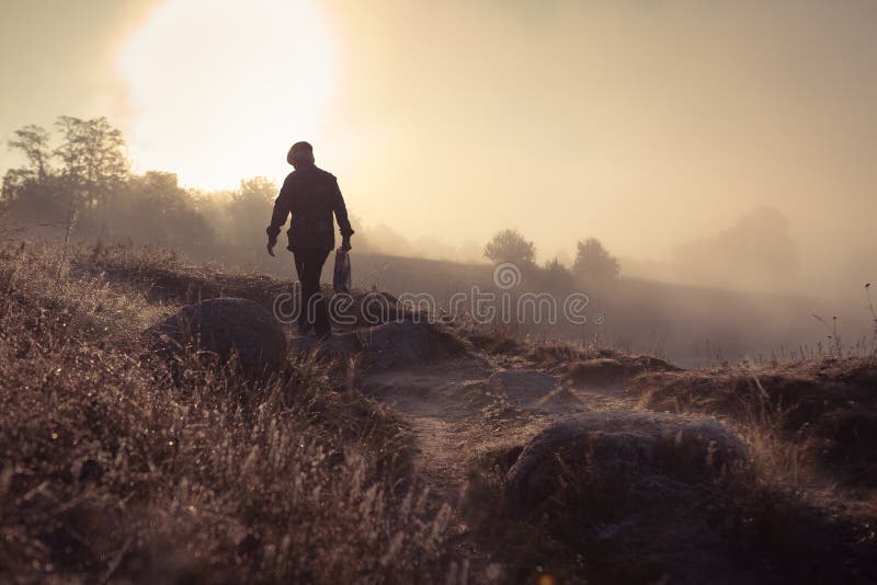 A misty morning by the lake. Silhouette of man walking away.