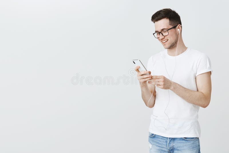Mit Liedern durch das Leben Porträt des glücklichen und erfüllten hübschen europäischen Mannes, der kühle Musik-APP auf Smartphon lizenzfreies stockfoto Mit Liedern durch das Leben Porträt des glücklichen und erfüllten hübschen europäischen Mannes, der kühle Musik-APP auf Smartphon lizenzfreies stockfoto