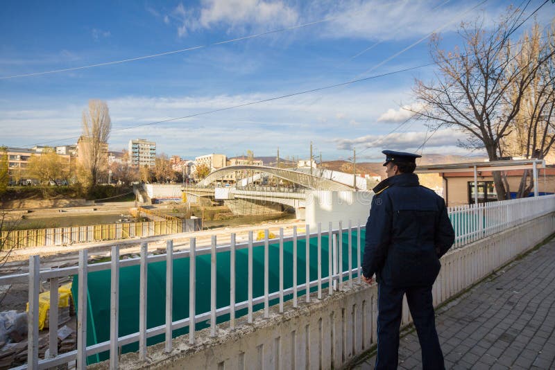 MITROVICA, KOSOVO - NOVEMBER 11, 2016: Kosovo Policeman watching the bridge on the Ibar river stock images MITROVICA, KOSOVO - NOVEMBER 11, 2016: Kosovo Policeman watching the bridge on the Ibar river stock images