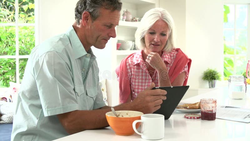 Mitte gealterte Paare, die Digital-Tablet über Frühstück betrachten