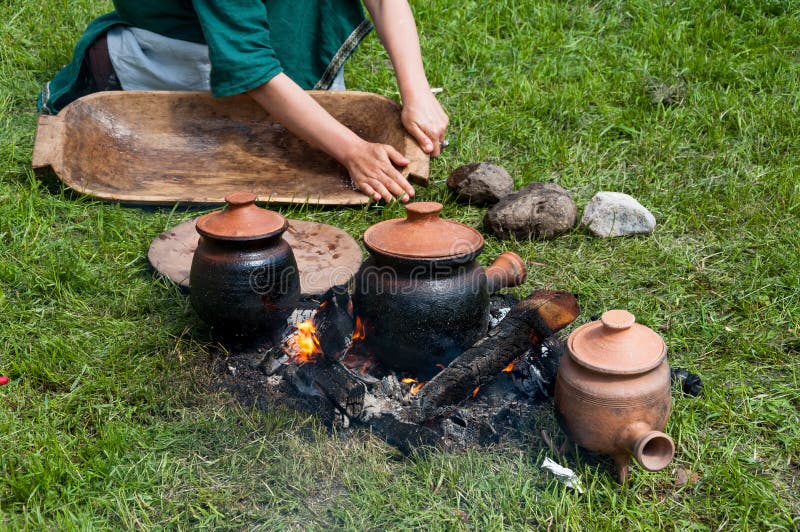 Medieval lifestyle scene - medieval pots and dishes being cooked on fire and girl washing the wooden bowl. Medieval lifestyle scene - medieval pots and dishes being cooked on fire and girl washing the wooden bowl