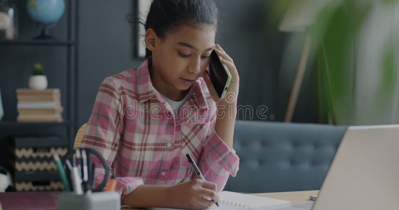 Mittelöstliche Schulmädchen, die auf dem Handy reden und Hausaufgaben in Notebook zu Hause machen