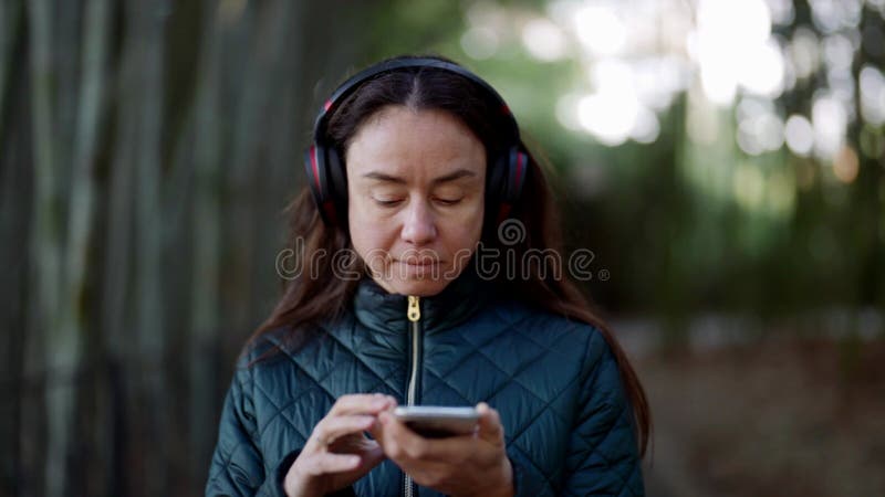 Mittlere Frau hört während des Spazierganges Lieblingslieder von drahtlosen Kopfhörern und Mobiltelefonen