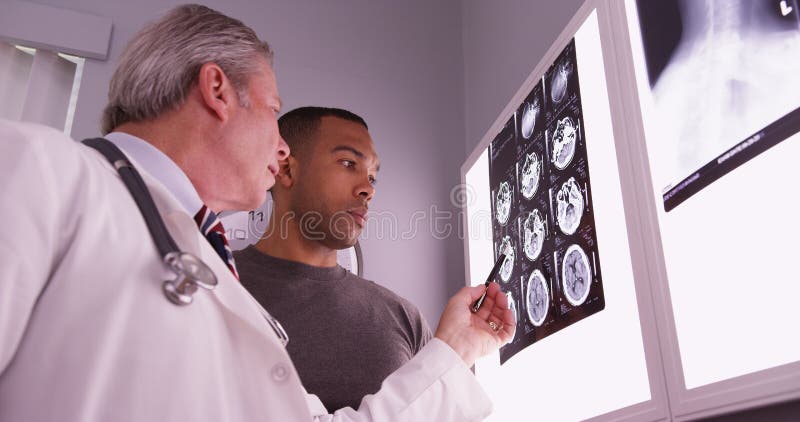 Mittlerer gealterter Arzt, der x-Strahl des afrikanischen Patienten wiederholt lizenzfreie stockbilder Mittlerer gealterter Arzt, der x-Strahl des afrikanischen Patienten wiederholt lizenzfreie stockbilder