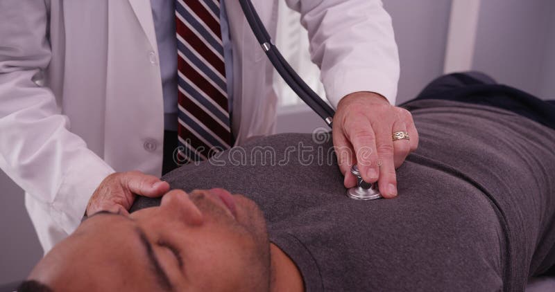 Mittlerer gealterter Doktor, der auf Lungen des schwarzen erwachsener Mannespatienten hört lizenzfreies stockfoto Mittlerer gealterter Doktor, der auf Lungen des schwarzen erwachsener Mannespatienten hört lizenzfreies stockfoto