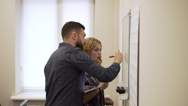 Mittlerer Schuss des jungen Mannes und Frau zeichnen ein Diagramm auf weißem Brett im Büro