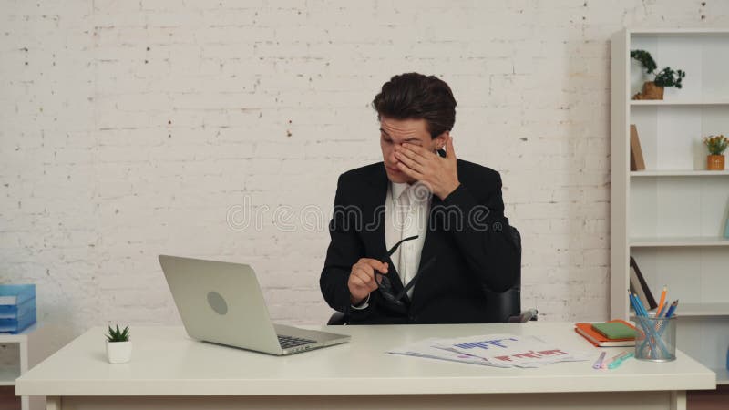 Mittleres Video eines jungen Mannes, der am Tisch im Büro sitzt und an einem Laptop arbeitet. er rieb sich müde die Augen und