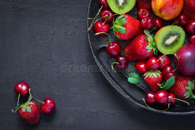 Mix of summer berries and fruits on a black plate. Top view with