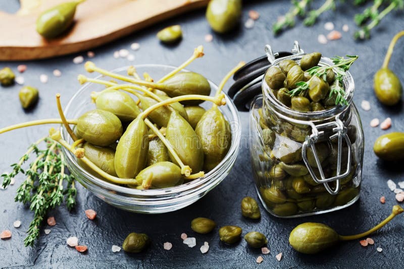 Mixed capers in jar and bowl on black kitchen table. royalty free stock image