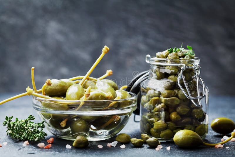 Mixed capers in jar and bowl on dark kitchen table. royalty free stock photo