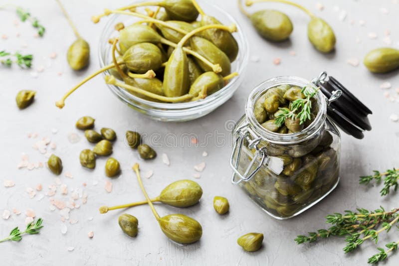 Mixed capers in jar and bowl on gray kitchen table from above. stock photos