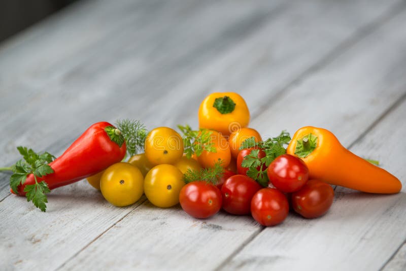 Mixed colored cherry tomatoes and mini paprika with fresh herbs on a wooden background stock photo Mixed colored cherry tomatoes and mini paprika with fresh herbs on a wooden background stock photo