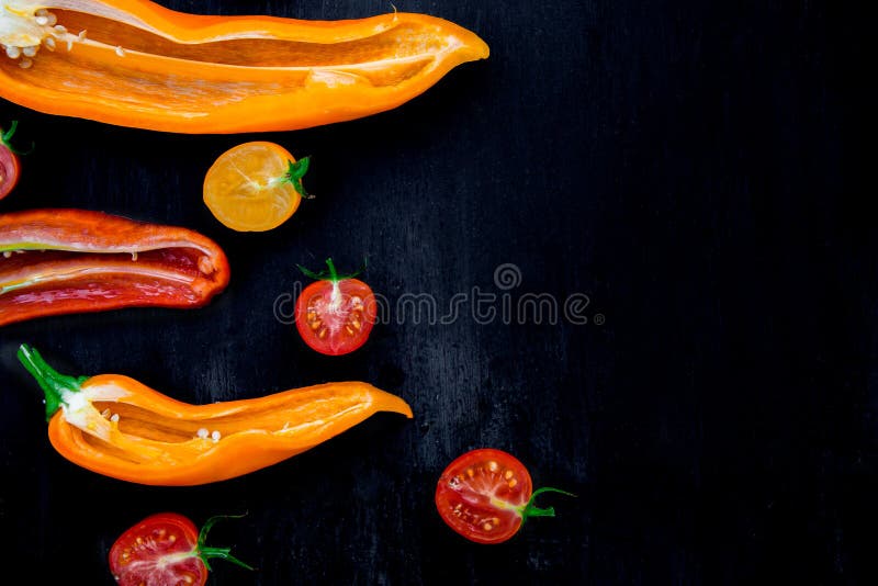 Mixed of half red and yellow pepper with a green branch near cherry tomato on black backround. Top view. Frame. Copy space.