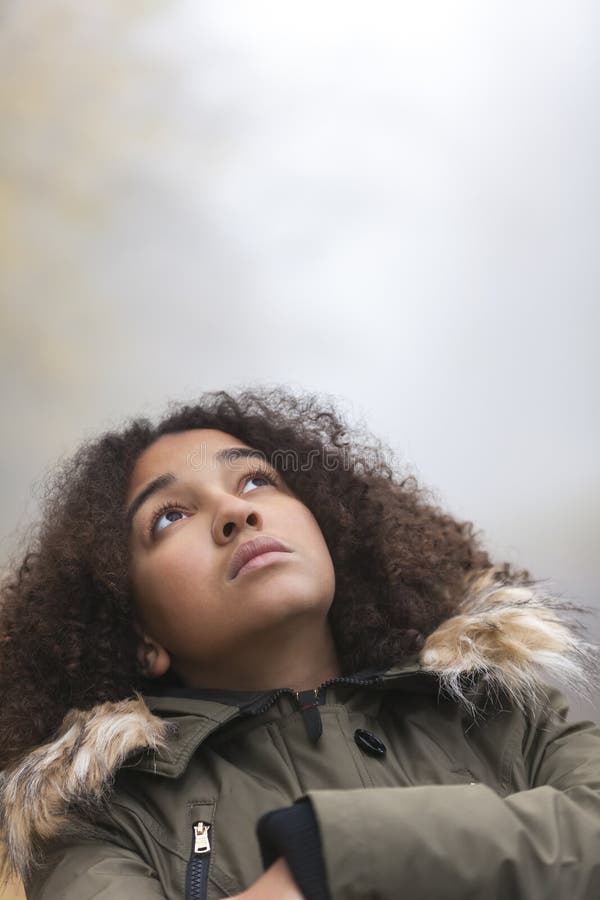 A beautiful thoughtful sad thinking mixed race African American girl or young woman looking up outside on a foggy or misty day. A beautiful thoughtful sad thinking mixed race African American girl or young woman looking up outside on a foggy or misty day