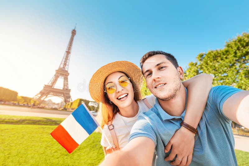 Couple in love hugging and taking selfie with french flag and Eiffel tower in the background. Honeymoon travel in