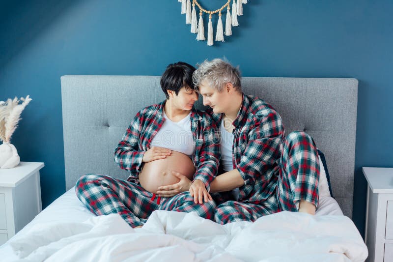 Mixed race couple are waiting for a baby. Husband and his pregnant wife in cozy pajamas relaxing on the bed at modern royalty free stock photos
