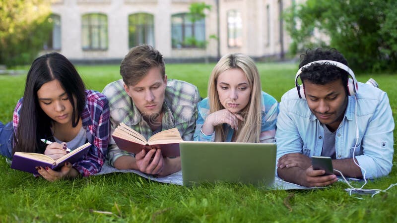Mixed-race students lying on grass and preparing for exams, university education stock photo Mixed-race students lying on grass and preparing for exams, university education stock photo