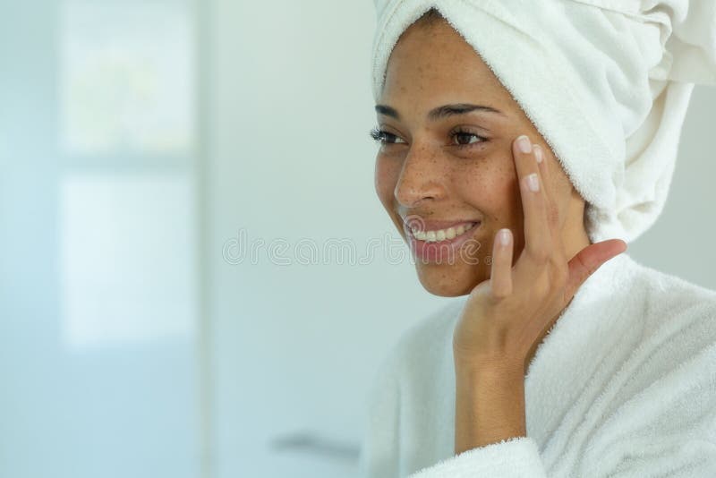 Mixed race woman wearing bathrobe and cleansing face mask in bathroom