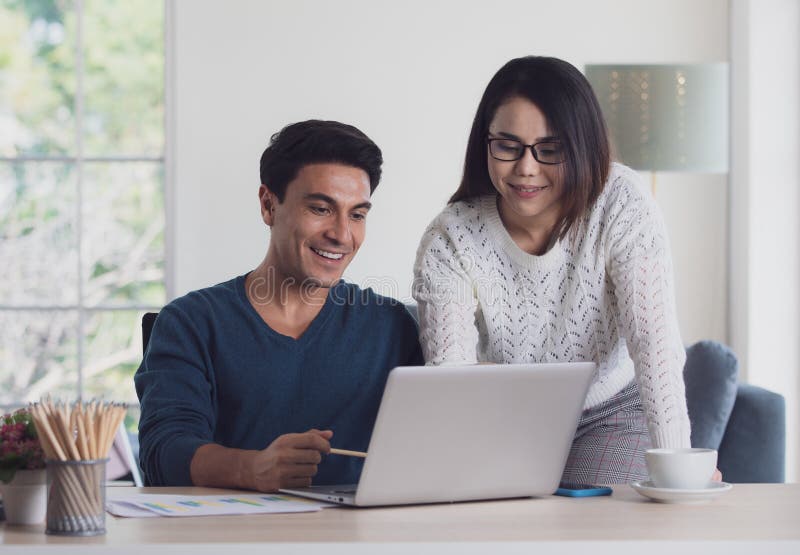 Mixed races couple family, Caucasian man and Asian woman, working together via laptop notebook computer and discussing in living