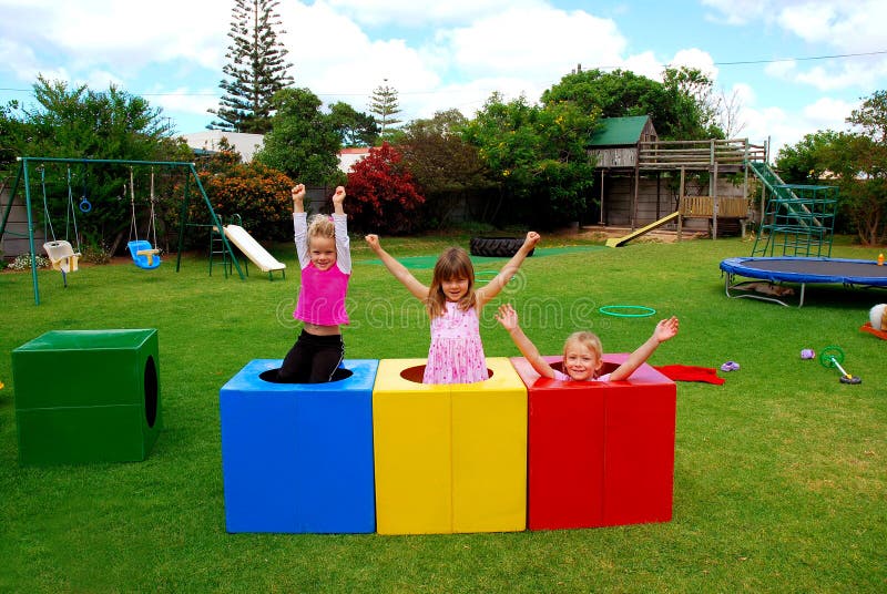 Three beautiful caucasian girls with happy smiling facial expressions playing in colorful boxes and raising up their arms in the air on the playground outdoors. Three beautiful caucasian girls with happy smiling facial expressions playing in colorful boxes and raising up their arms in the air on the playground outdoors