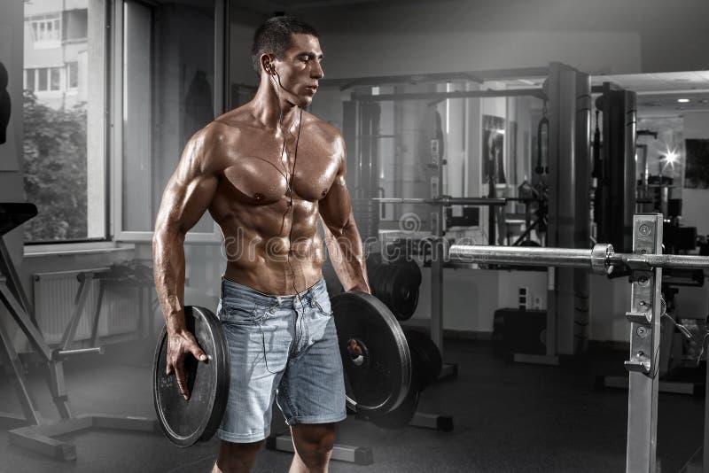 Mięśniowy mężczyzna pracujący w gym z barbell out, kształtny brzuszny Silny męski nagi półpostaci abs obraz stock Mięśniowy mężczyzna pracujący w gym z barbell out, kształtny brzuszny Silny męski nagi półpostaci abs obraz stock