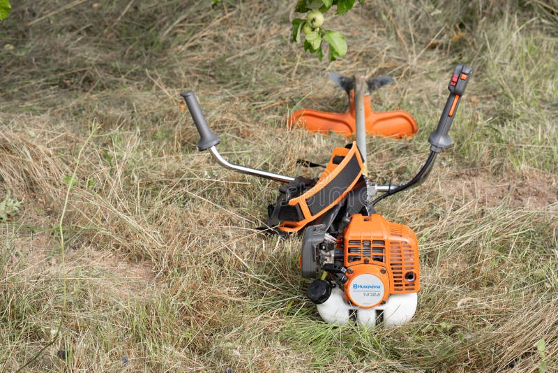 Minsk, Belarus - 02/08/2020 Petrol scythe trimmer brushcutter Husqvarna 143R-II lies on the mown hay after mowing tall grass in the garden of a country house. Minsk, Belarus - 02/08/2020 Petrol scythe trimmer brushcutter Husqvarna 143R-II lies on the mown hay after mowing tall grass in the garden of a country house