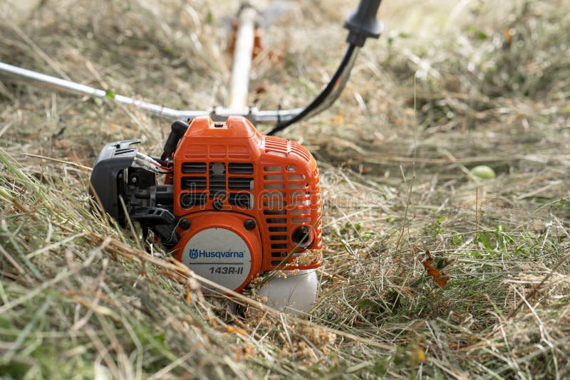 Minsk, Belarus - 02/08/2020 Petrol scythe trimmer brushcutter Husqvarna 143R-II lies on the mown hay after mowing tall grass in the garden of a country house. Minsk, Belarus - 02/08/2020 Petrol scythe trimmer brushcutter Husqvarna 143R-II lies on the mown hay after mowing tall grass in the garden of a country house