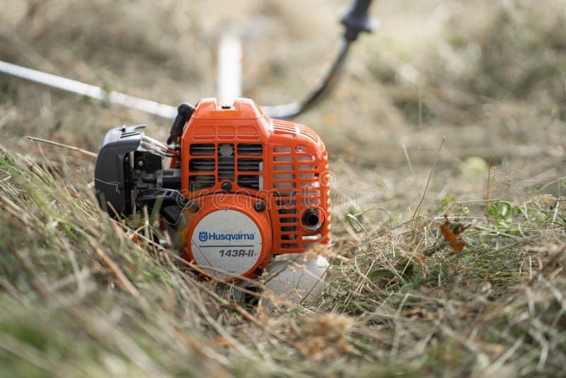 Minsk, Belarus - 02/08/2020 Petrol scythe trimmer brushcutter Husqvarna 143R-II lies on the mown hay after mowing tall grass in the garden of a country house. Minsk, Belarus - 02/08/2020 Petrol scythe trimmer brushcutter Husqvarna 143R-II lies on the mown hay after mowing tall grass in the garden of a country house