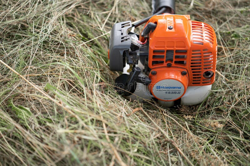 Minsk, Belarus - 02/08/2020 Petrol scythe trimmer brushcutter Husqvarna 143R-II lies on the mown hay after mowing tall grass in the garden of a country house. Minsk, Belarus - 02/08/2020 Petrol scythe trimmer brushcutter Husqvarna 143R-II lies on the mown hay after mowing tall grass in the garden of a country house