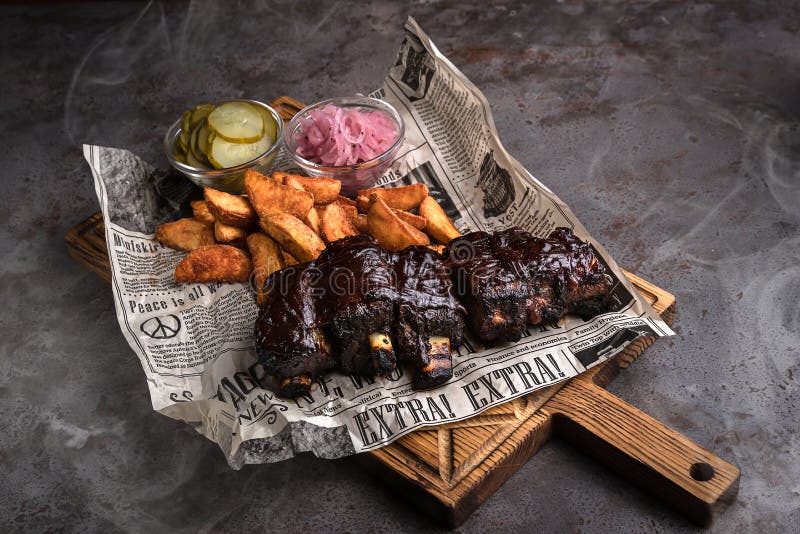 Mińsk, Białoruś - sierpień, 2019 żebra wieprzowe BBQ z pieczonym ziemniakiem i ogórkiem serwują gazety na drewnianym tle zdjęcie stock Mińsk, Białoruś - sierpień, 2019 żebra wieprzowe BBQ z pieczonym ziemniakiem i ogórkiem serwują gazety na drewnianym tle zdjęcie stock